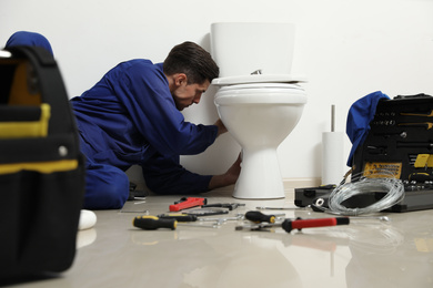 Professional plumber working with toilet bowl in bathroom