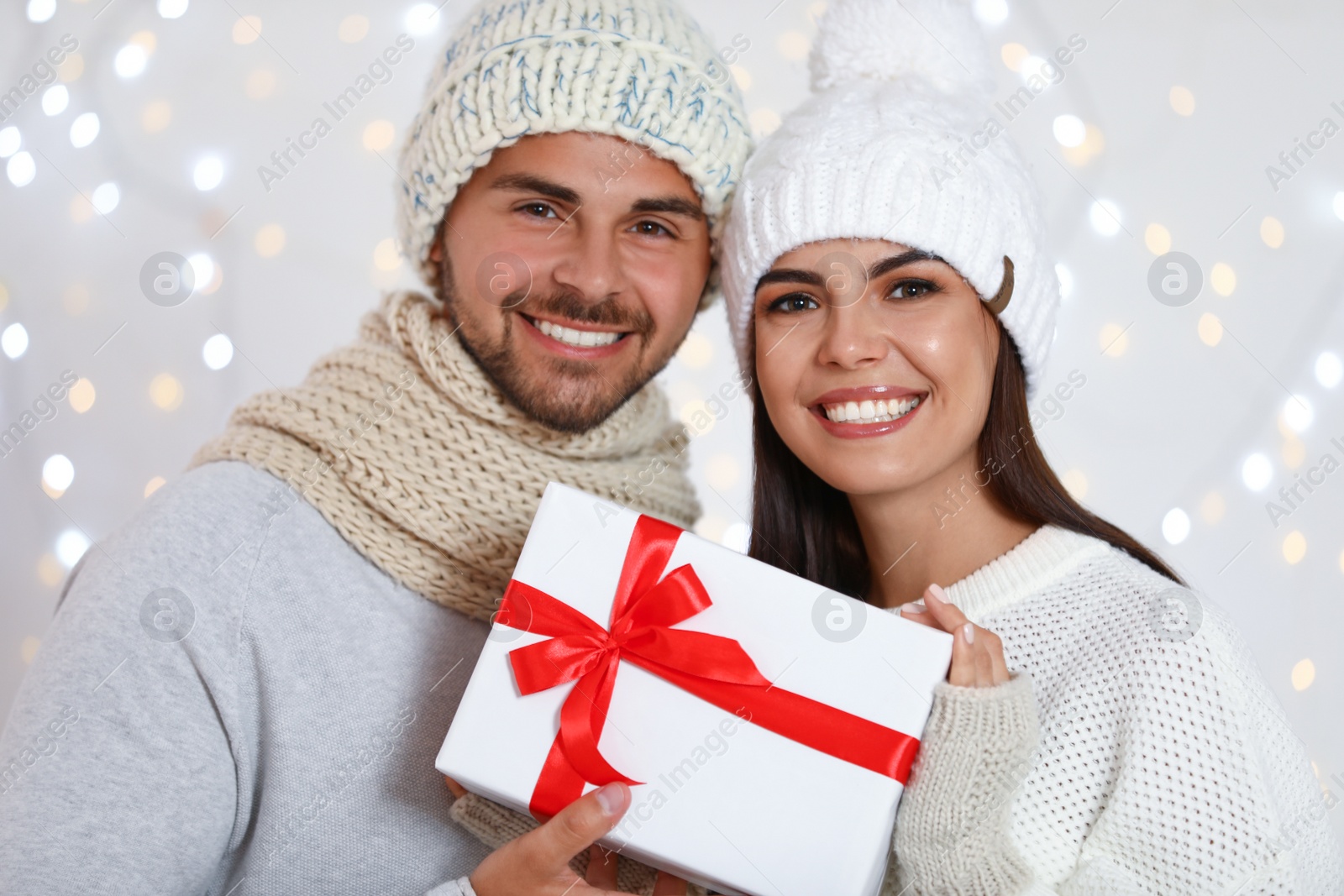 Photo of Lovely young couple with gift box against blurred festive lights. Christmas celebration