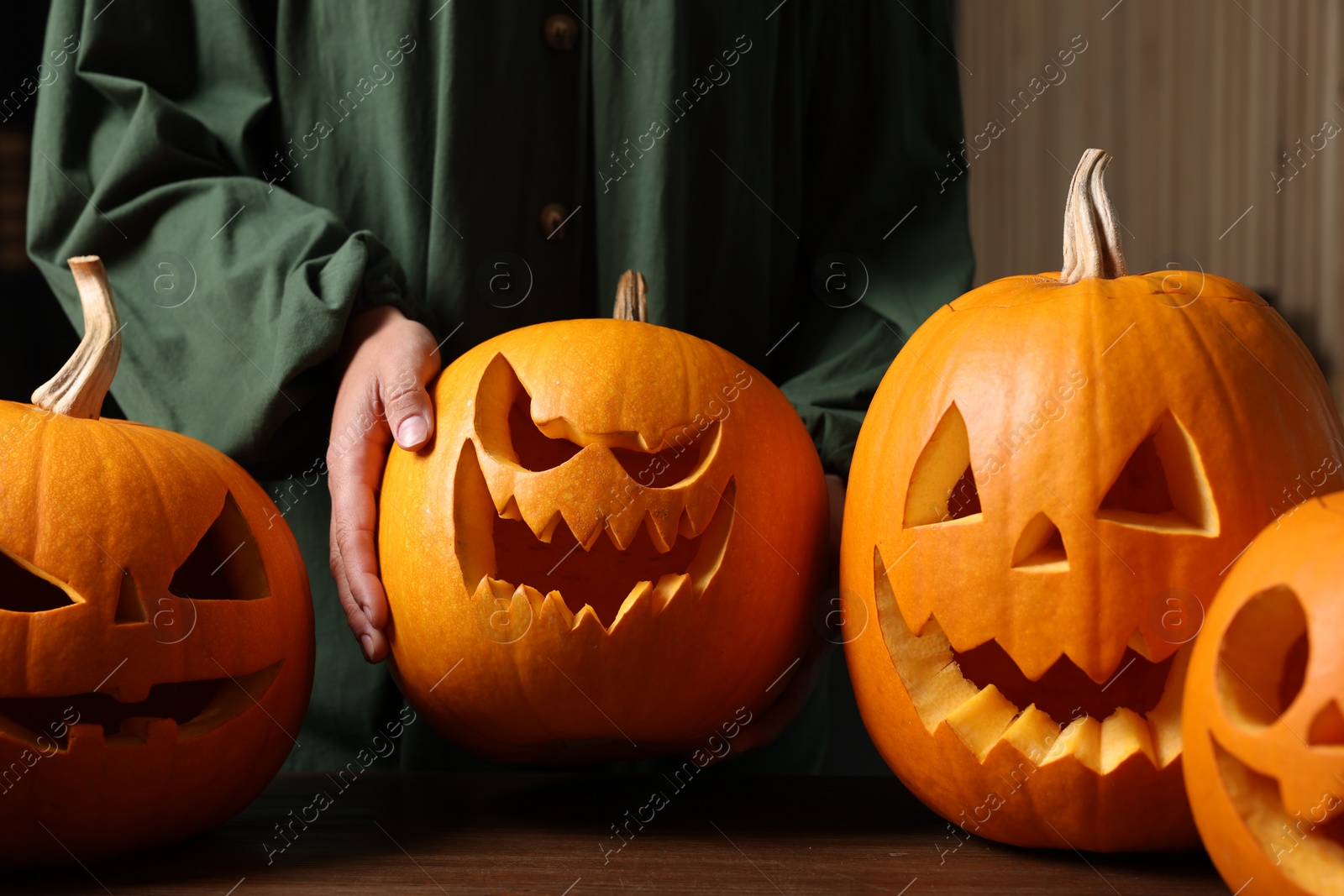 Photo of Woman with carved pumpkins for Halloween at wooden table, closeup