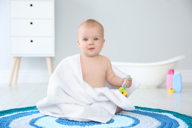 Photo of Cute little baby with soft towel and rattle on rug in bathroom