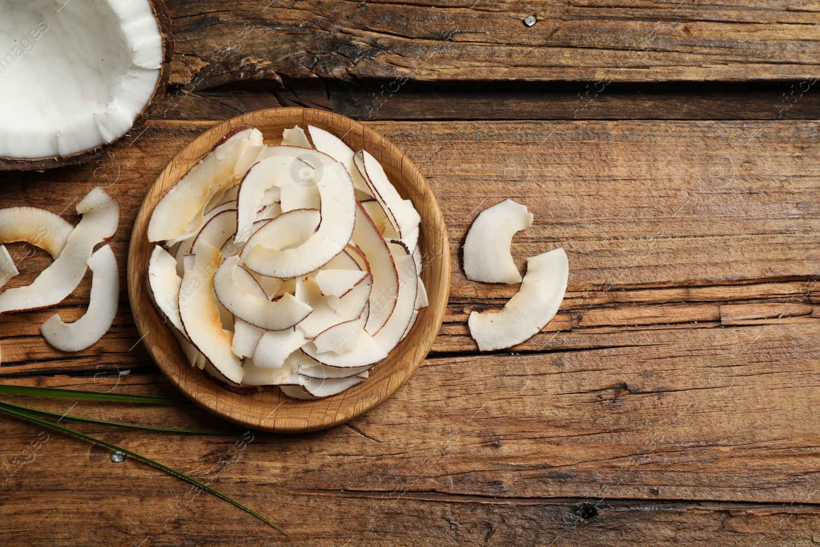 Photo of Tasty coconut chips on wooden table, flat lay