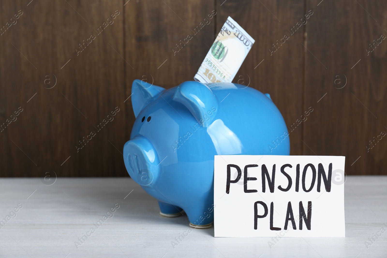 Photo of Card with phrase Pension Plan, piggy bank and dollar banknote on white wooden table. Retirement concept