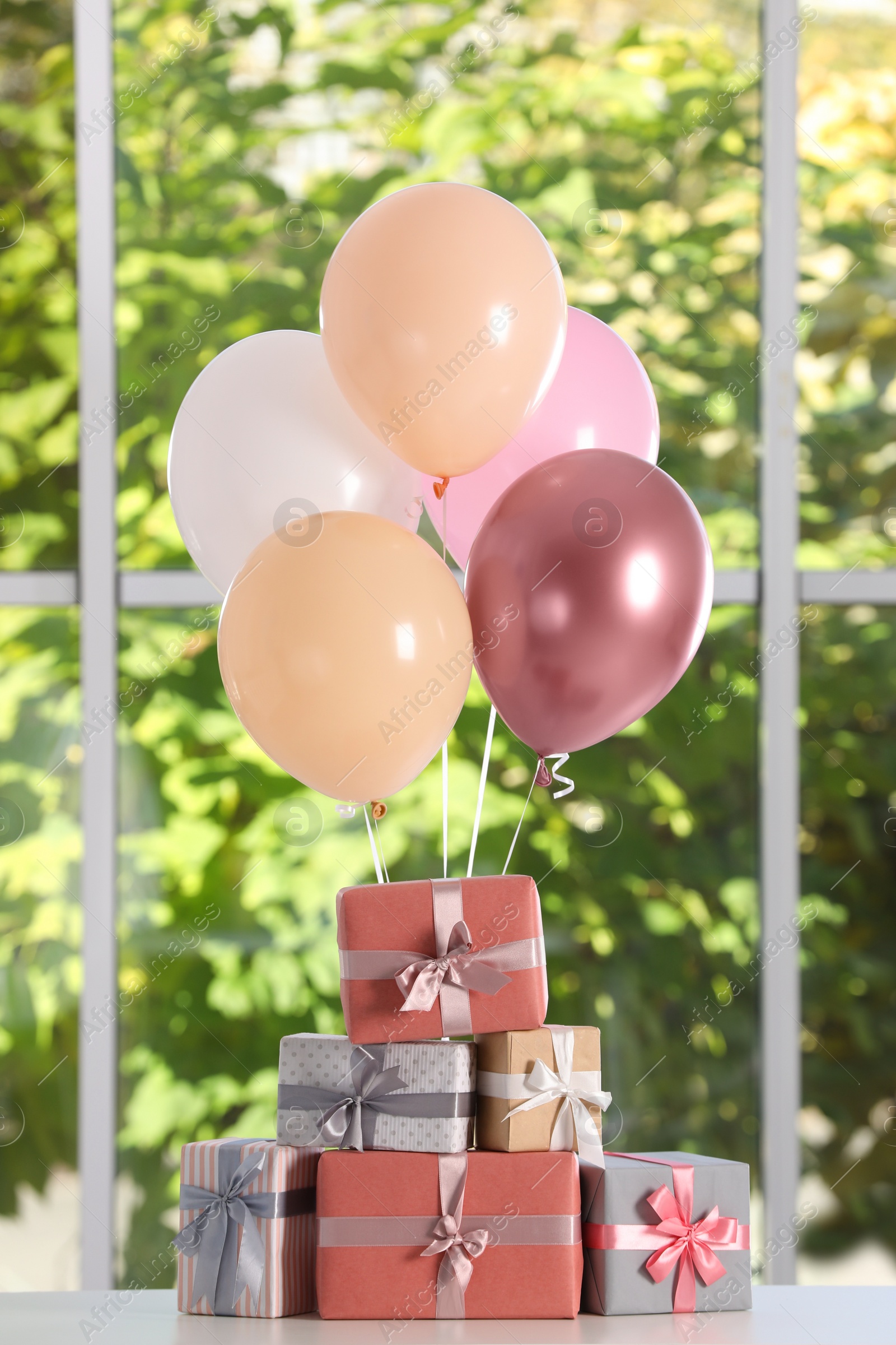 Photo of Bunch of color balloons and beautifully wrapped gift boxes on white table near window