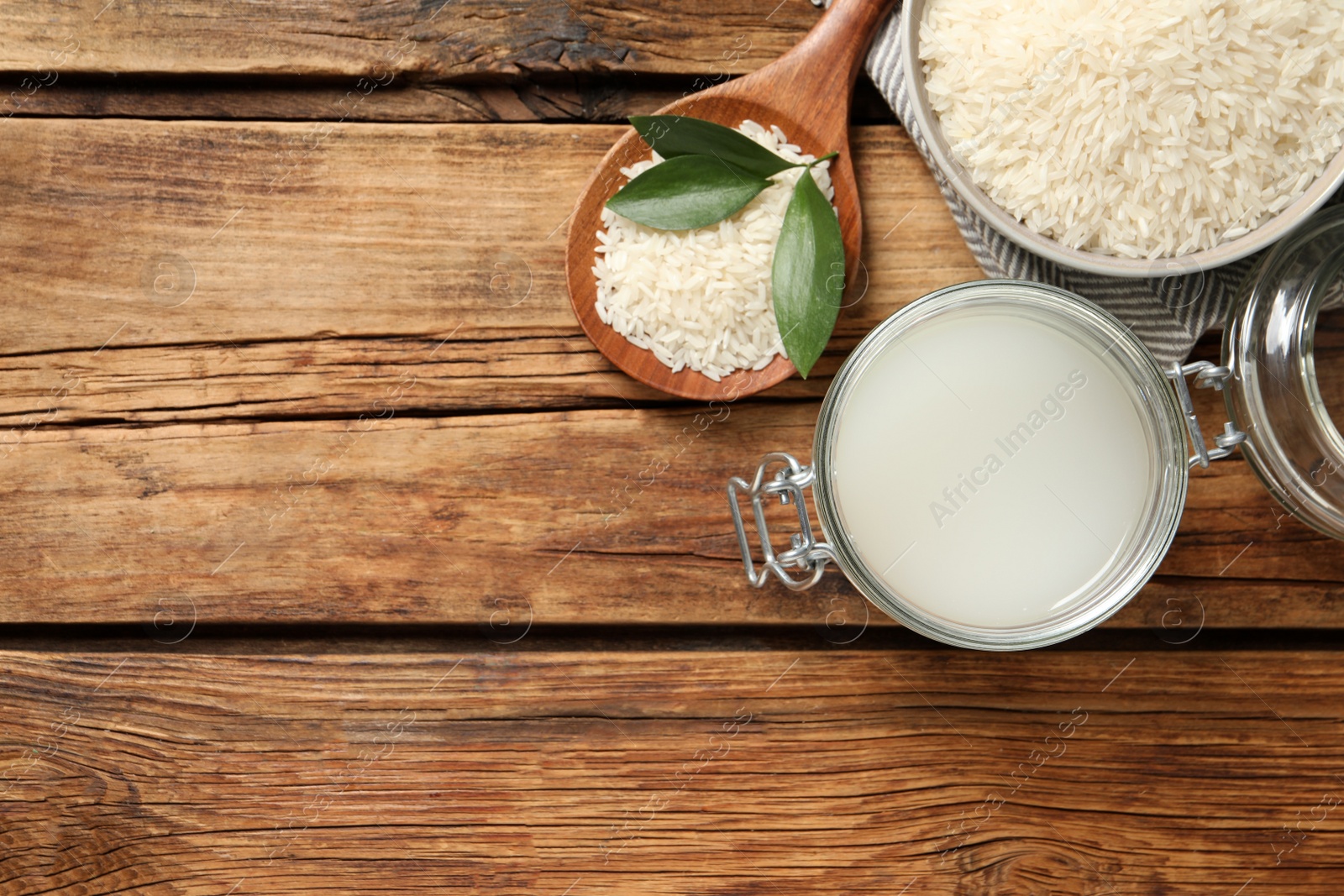 Photo of Glass jar with rice water and grains on wooden table, flat lay. Space for text