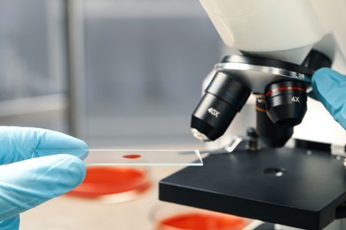 Photo of Scientist examining sample of red liquid on slide under microscope in laboratory, closeup