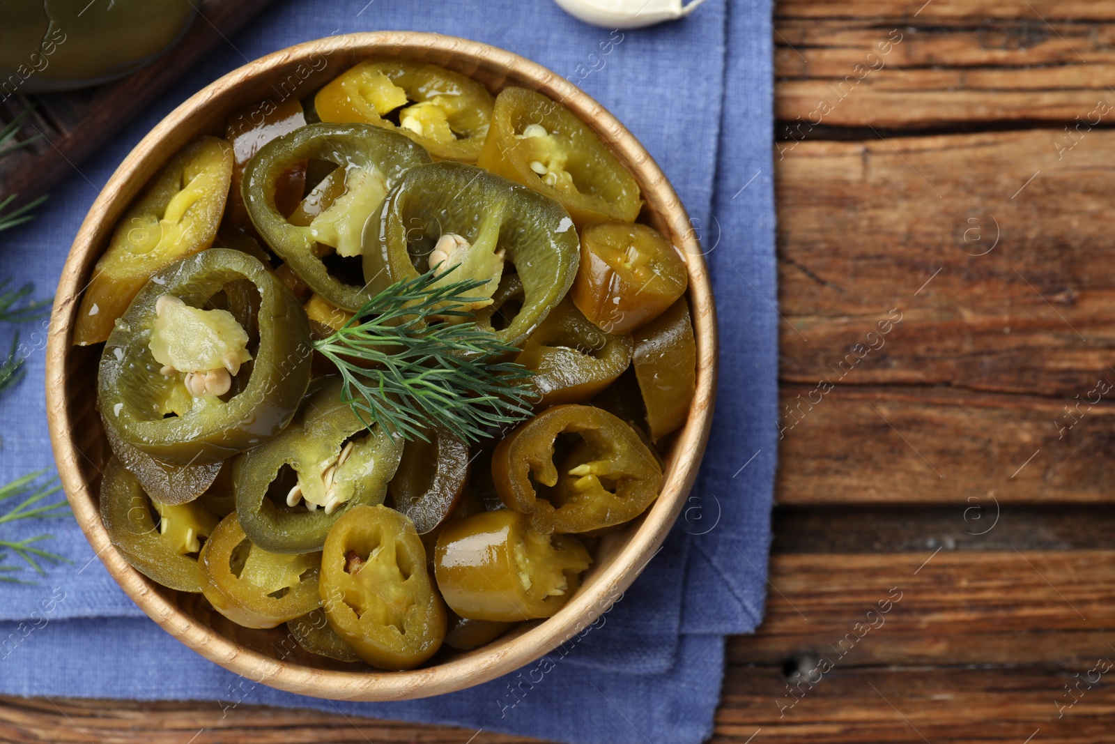 Photo of Bowl with slices of pickled green jalapeno peppers on wooden table, top view. Space for text