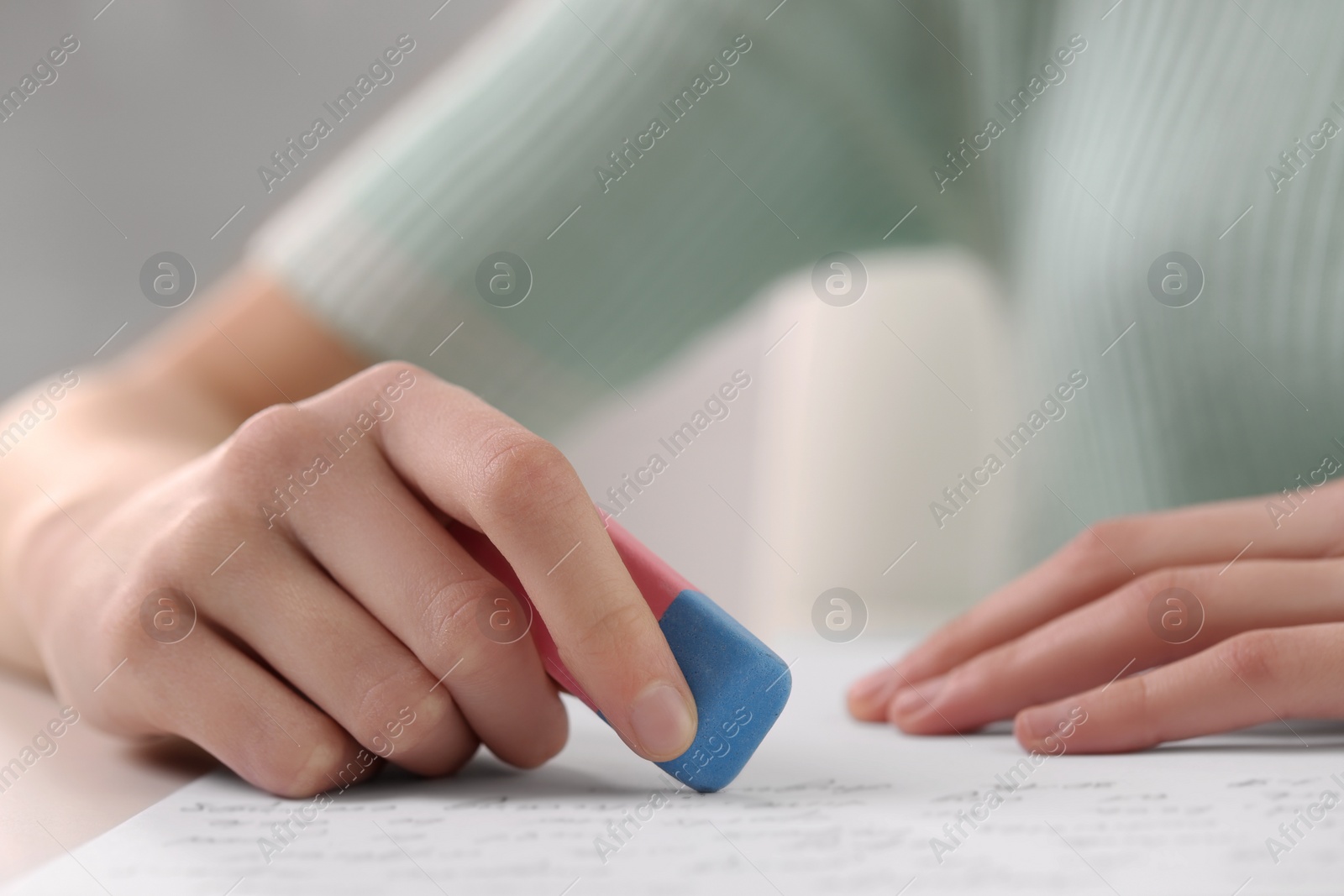 Photo of Girl erasing mistake in her notebook at white desk, closeup