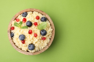 Photo of Bowl of tasty couscous with blueberries, pomegranate and mint on green background, top view. Space for text