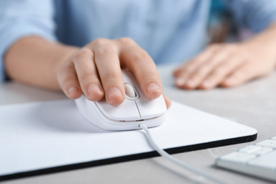 Photo of Woman using wired computer mouse on pad at light grey marble table, closeup