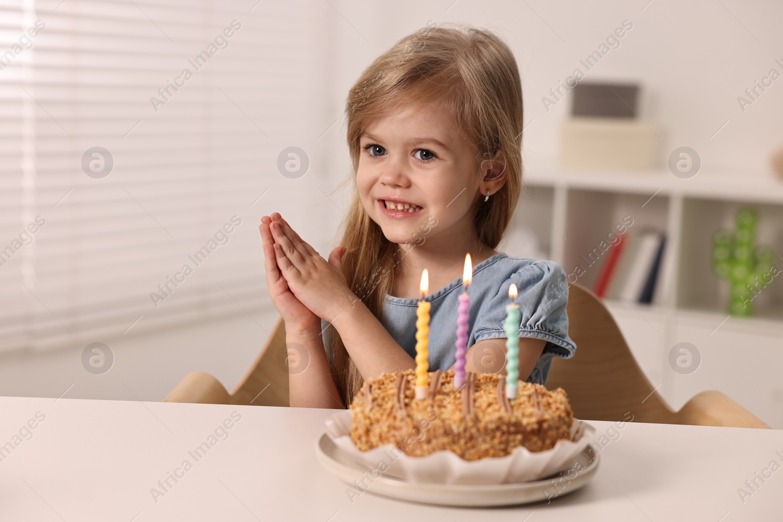 Photo of Cute girl with birthday cake at table indoors