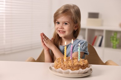 Cute girl with birthday cake at table indoors