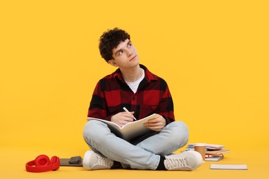 Photo of Portrait of student with notebook and stationery sitting on orange background