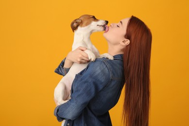 Photo of Woman kissing cute Jack Russell Terrier dog on orange background