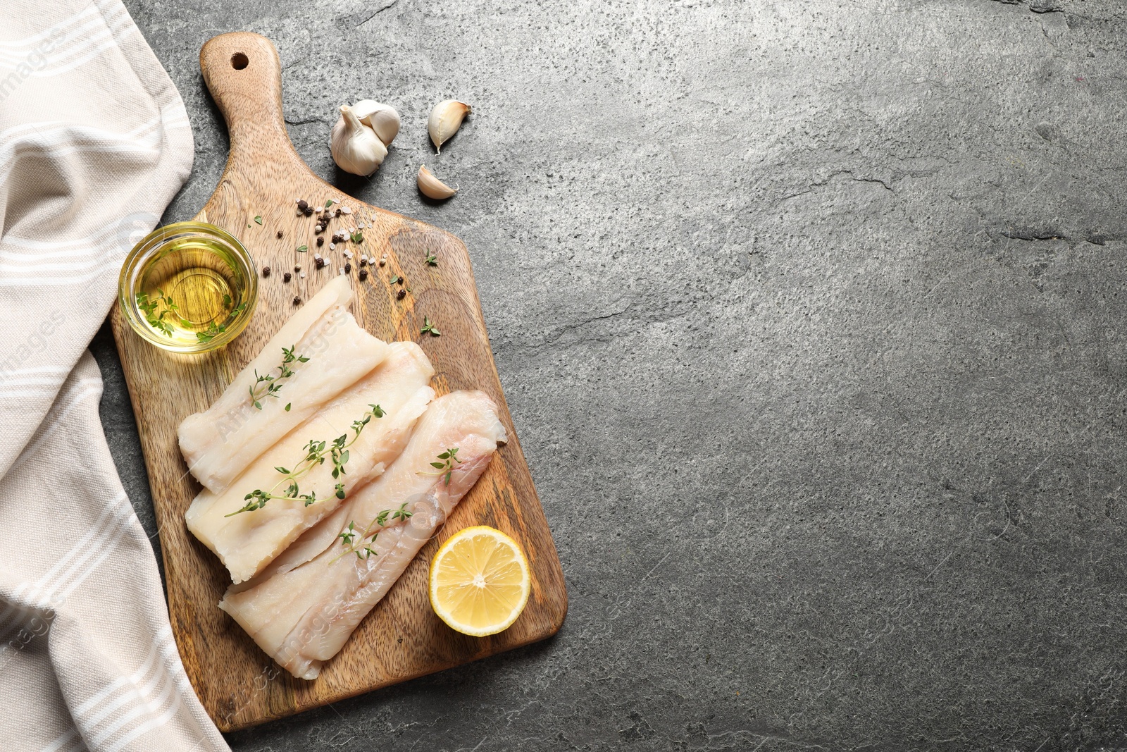 Photo of Raw cod fish, microgreens, oil, spices and lemon on grey textured table, top view. Space for text