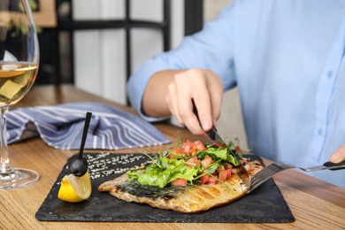 Photo of Woman eating delicious grilled fish at wooden table indoors, closeup