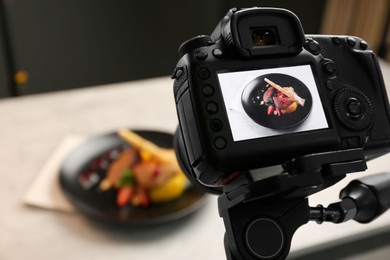 Photo of Professional camera with picture of baked chicken, parsnip and strawberries on white table in photo studio, closeup. Food photography