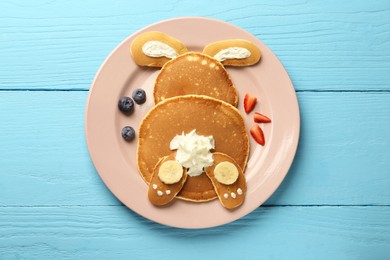 Creative serving for kids. Plate with cute bunny made of pancakes, berries, cream and banana on light blue wooden table, top view