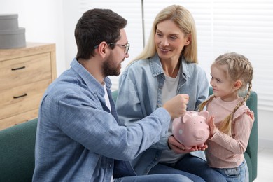 Planning budget together. Little girl with her parents putting coin into piggybank at home