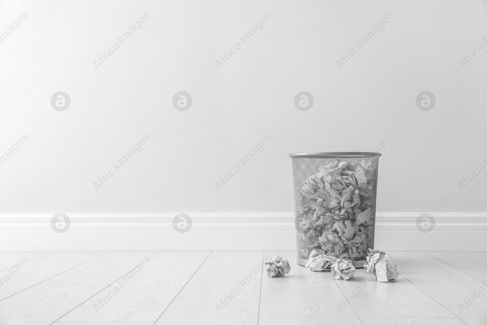 Photo of Metal bin and crumpled paper against light wall, space for text