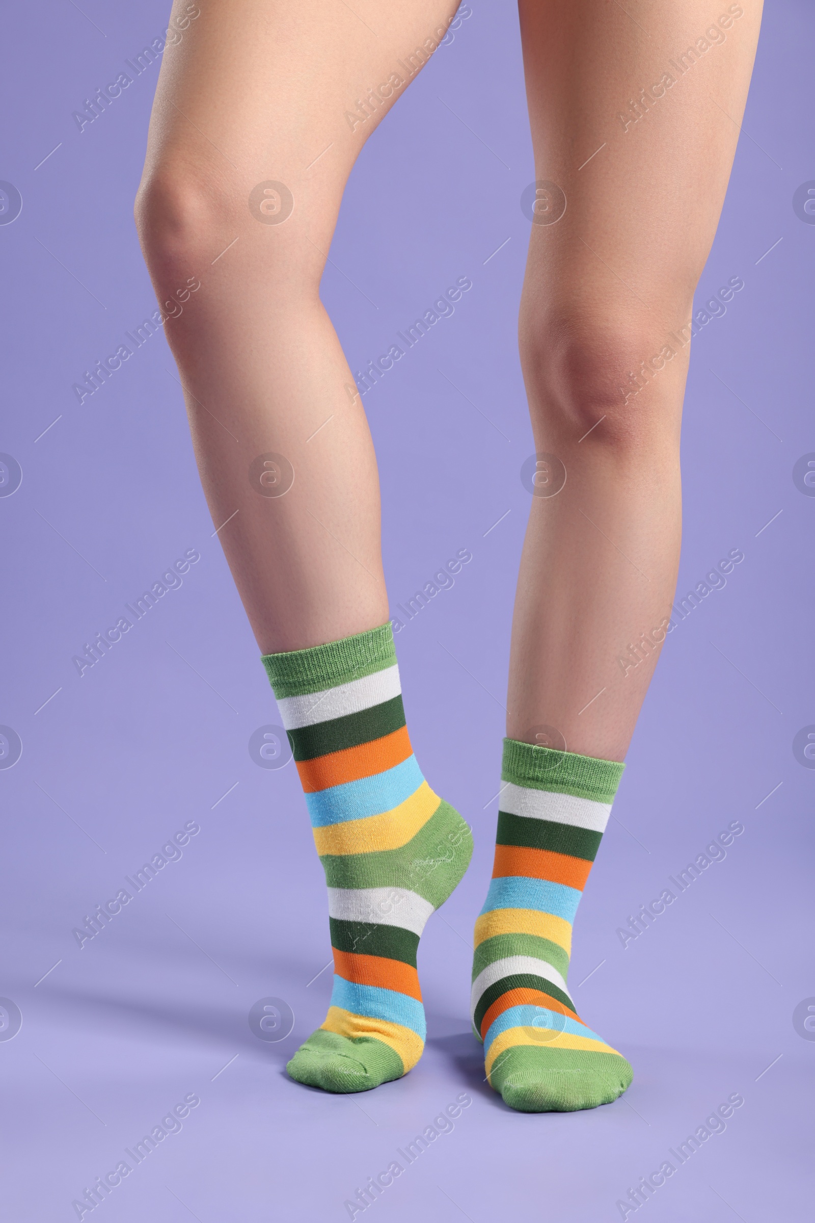 Photo of Woman in stylish colorful socks on violet background, closeup