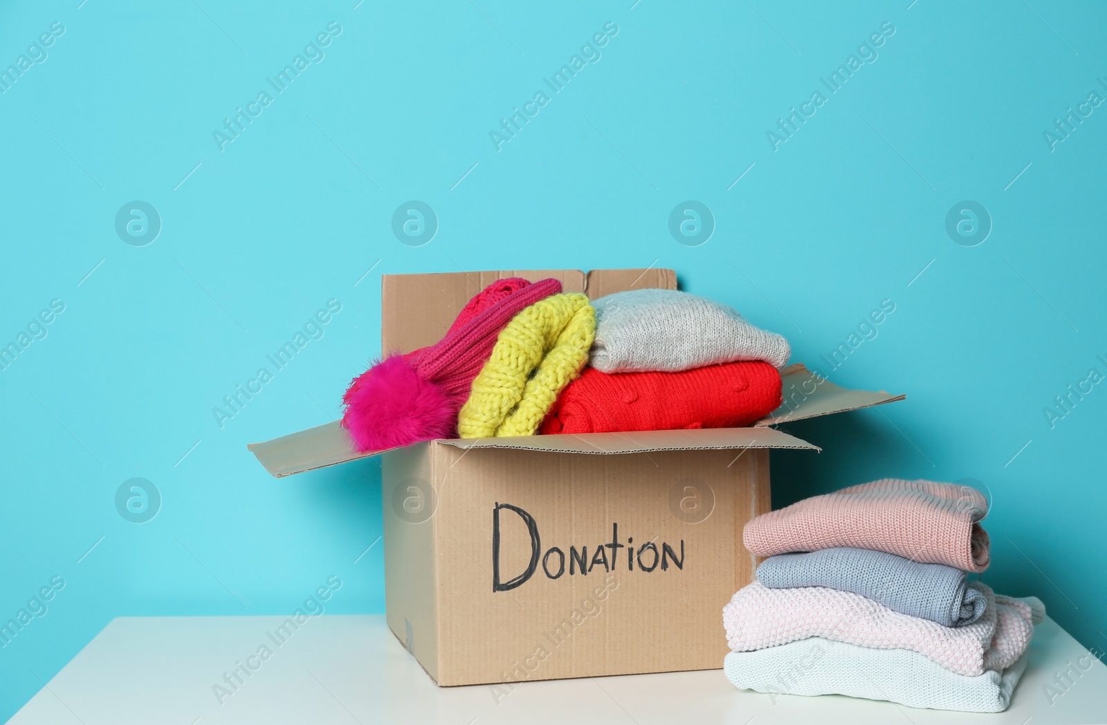 Photo of Donation box and knitted clothes on table against color background