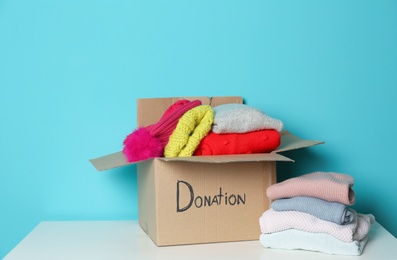Donation box and knitted clothes on table against color background