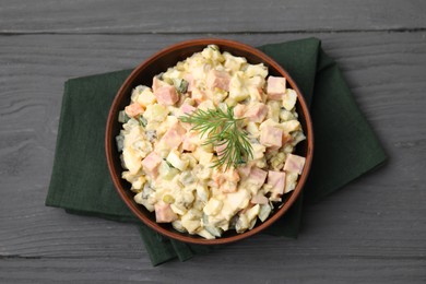 Photo of Tasty Olivier salad with boiled sausage in bowl on grey wooden table, top view