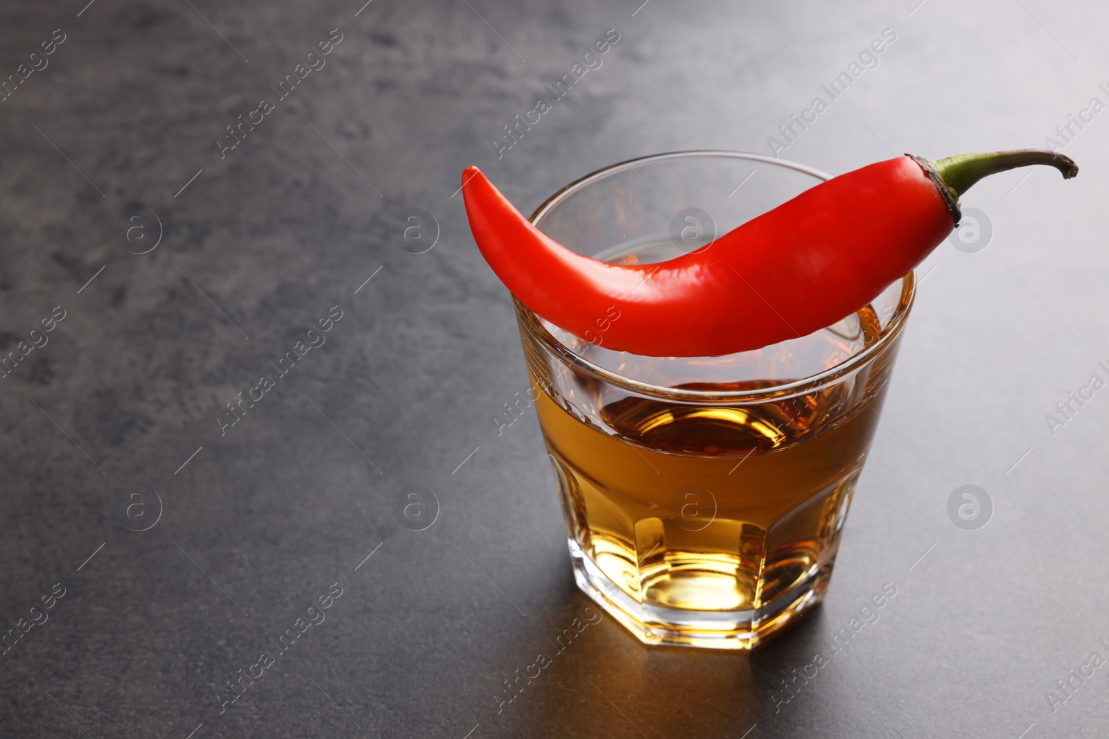 Photo of Red hot chili pepper and vodka in glass on grey table, space for text