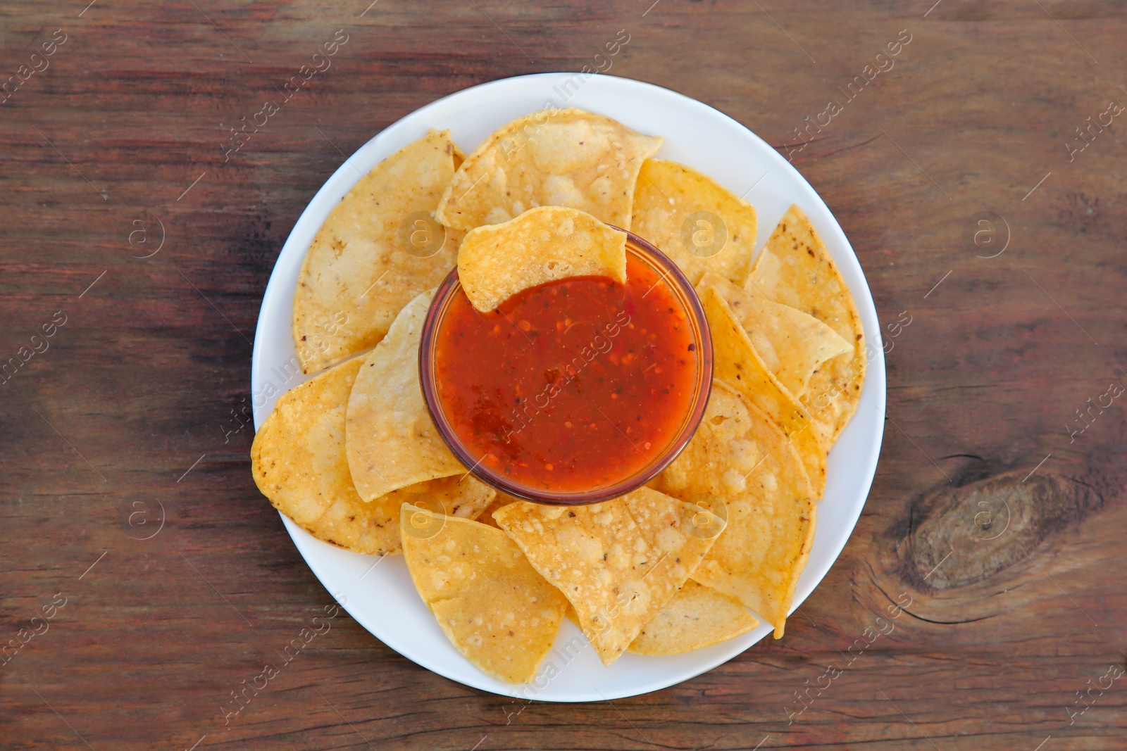 Photo of Tasty salsa sauce and tortilla chips on wooden table, top view