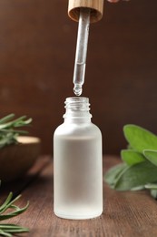 Photo of Dripping herbal essential oil from pipette into bottle on wooden table, closeup
