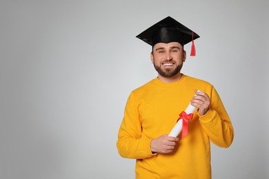 Photo of Happy student with graduation hat and diploma on grey background. Space for text