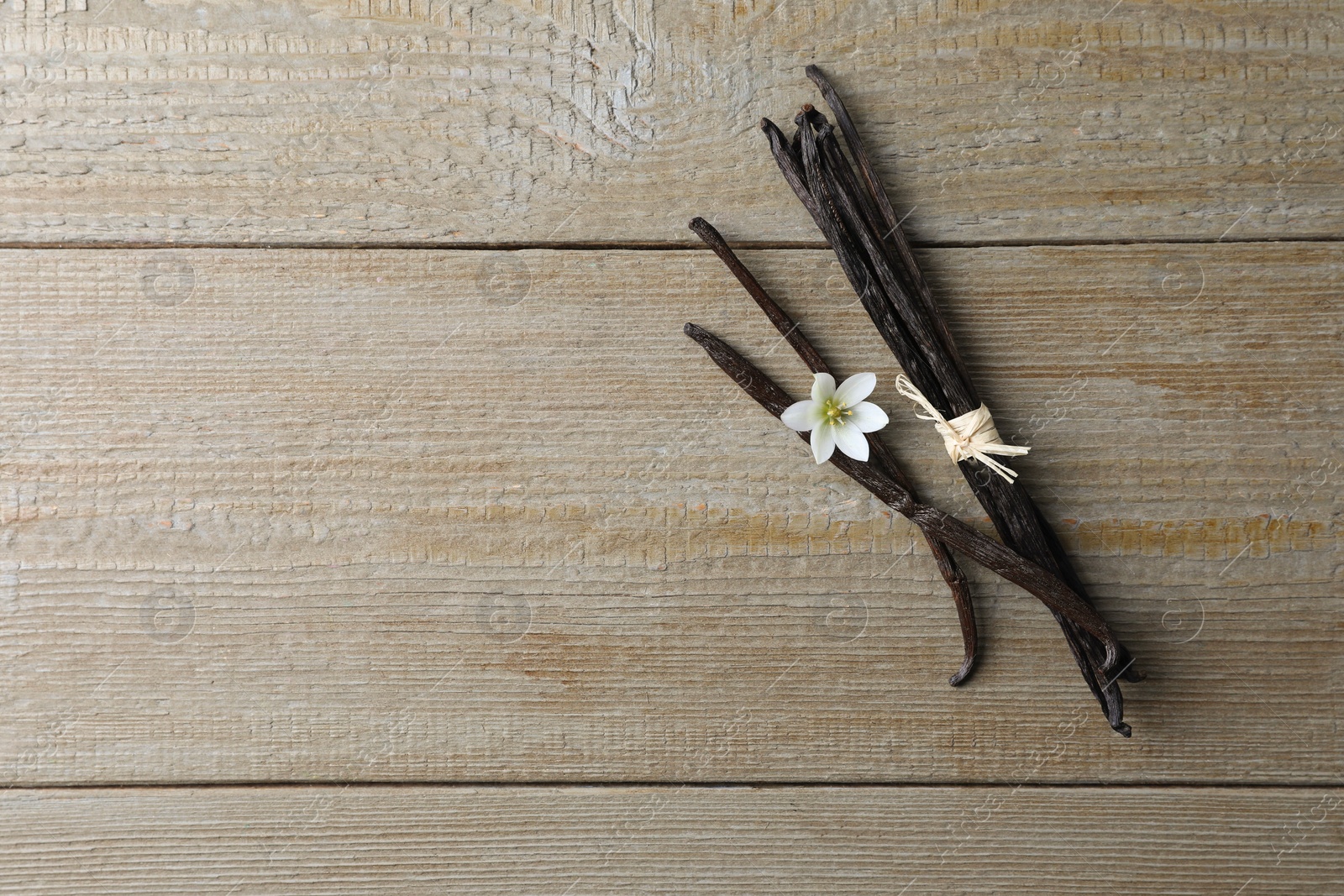 Photo of Vanilla pods and flower on wooden table, flat lay. Space for text