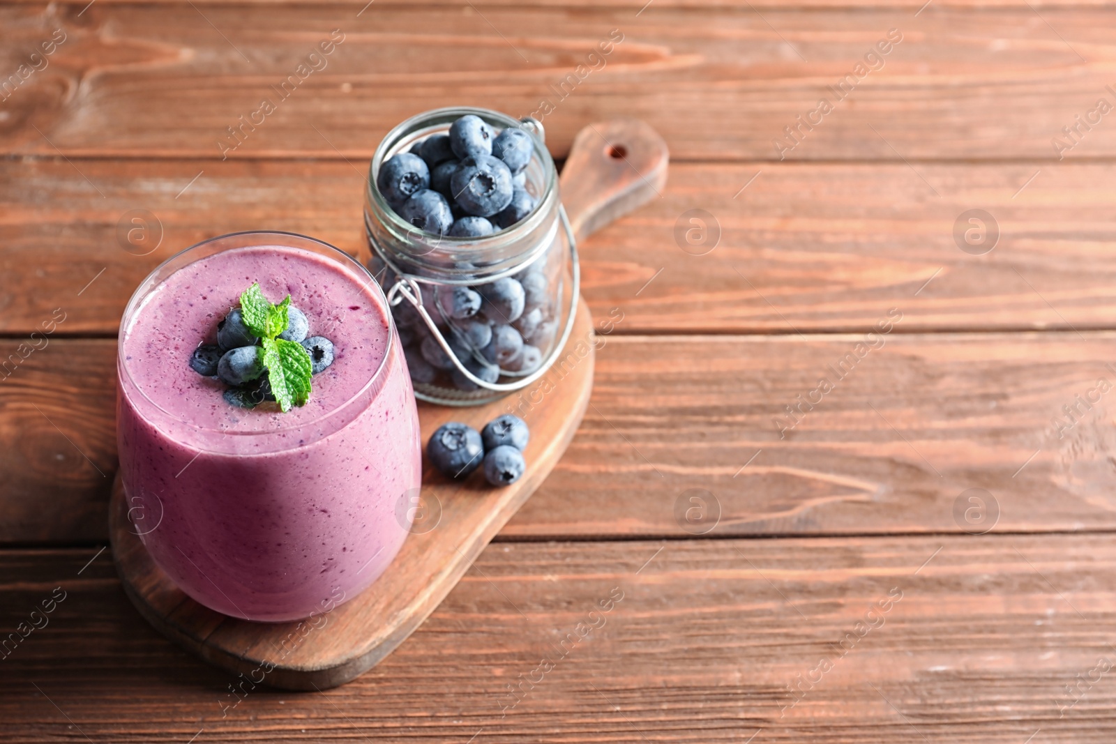 Photo of Glass of smoothie and jar with blueberries on wooden background. Space for text