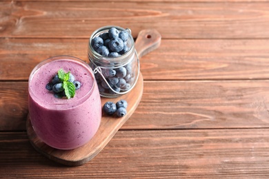 Glass of smoothie and jar with blueberries on wooden background. Space for text