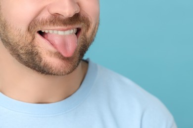 Photo of Man showing his tongue on light blue background, closeup. Space for text
