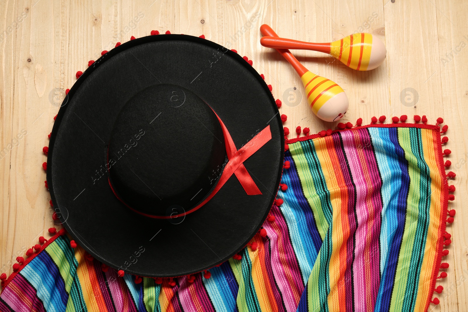 Photo of Mexican sombrero hat, maracas and colorful poncho on wooden background, flat lay