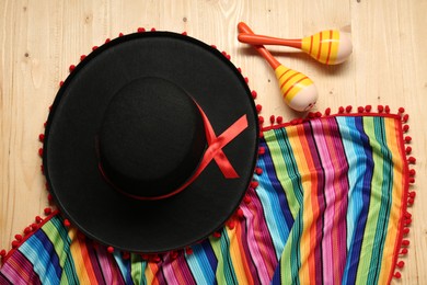 Photo of Mexican sombrero hat, maracas and colorful poncho on wooden background, flat lay