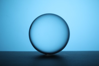 Photo of Transparent glass ball on table against light blue background