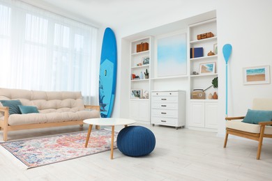 SUP board, shelving unit with different decor elements, table and pouf in room. Interior design