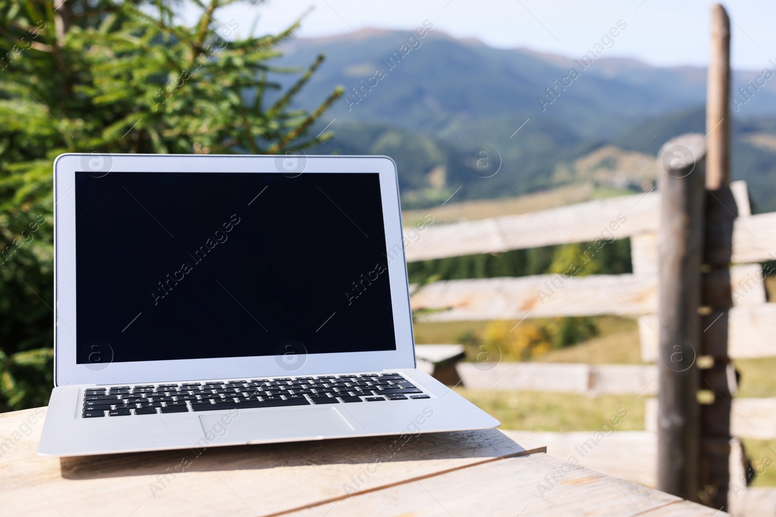 Photo of Laptop on wooden table in mountains, space for text. Distance work