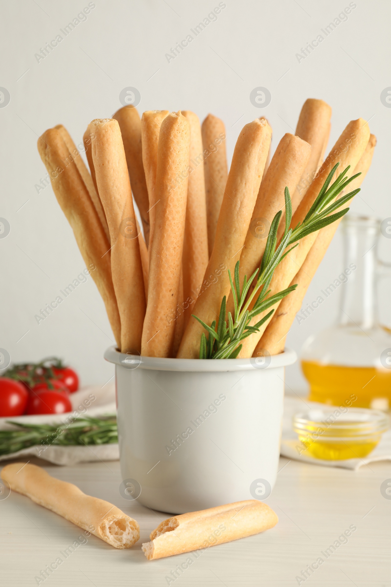 Photo of Delicious grissini sticks, oil, rosemary and tomatoes on white wooden table