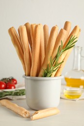Delicious grissini sticks, oil, rosemary and tomatoes on white wooden table