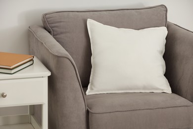 Photo of Soft white pillow on armchair and bedside table near light wall indoors