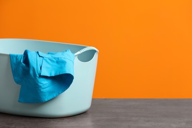 Photo of Plastic laundry basket with clothes near orange wall. Space for text