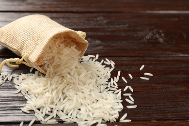 Photo of Raw basmati rice and bag on wooden table, space for text