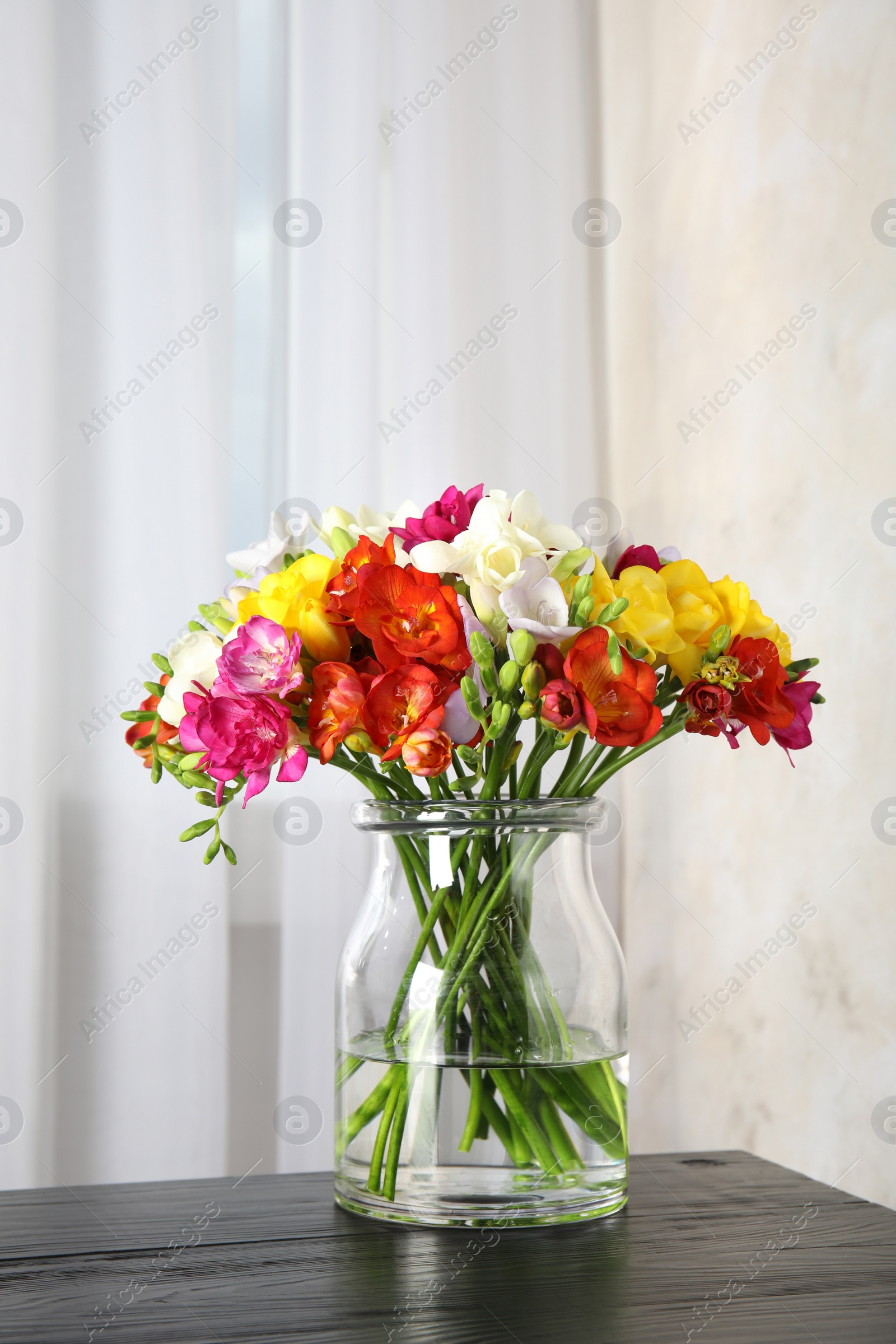 Photo of Vase with bouquet of spring freesia flowers on table in room