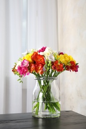 Vase with bouquet of spring freesia flowers on table in room