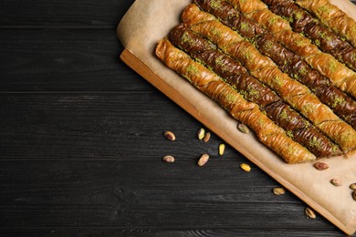 Photo of Delicious sweet baklava with pistachios on black wooden table, flat lay. Space for text