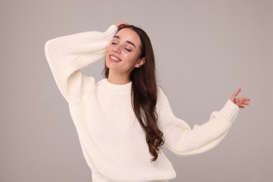 Beautiful young woman in stylish warm sweater on grey background