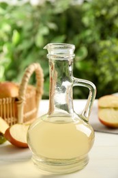 Photo of Natural apple vinegar on white table against blurred background